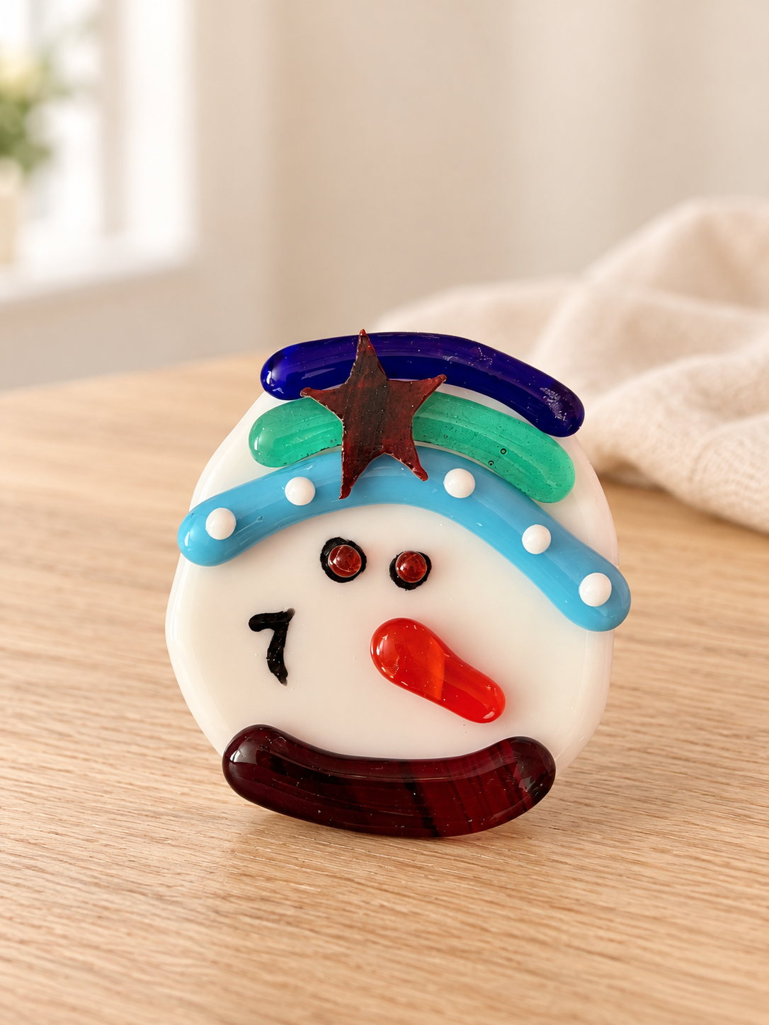 White glass snowman face with an orange nose and a turquoise and blue winter hat