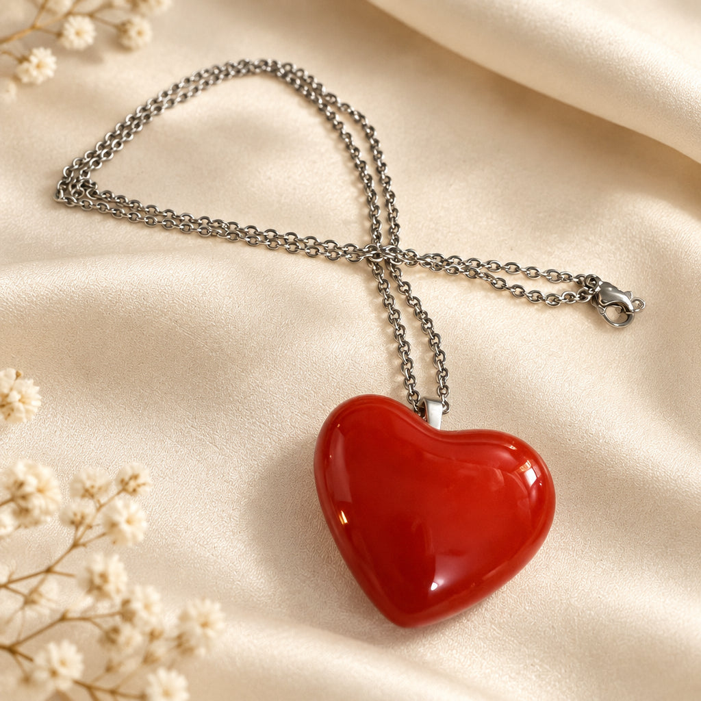 Solid red glass heart pendant on a silver-tone chain, displayed on cream fabric