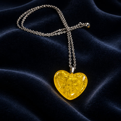 Translucent yellow glass heart pendant on a silver-tone chain against dark blue fabric