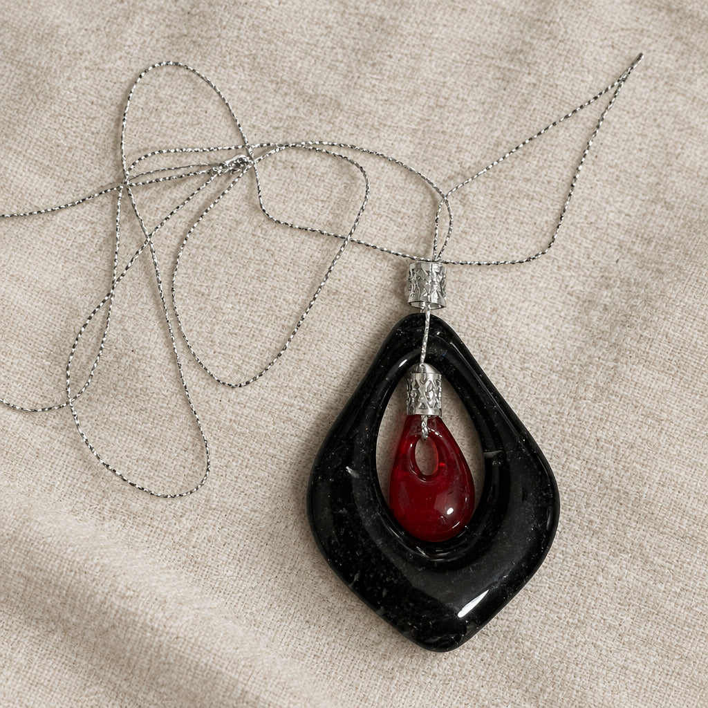 Black teardrop-shaped openwork glass pendant with red center detail on a chain