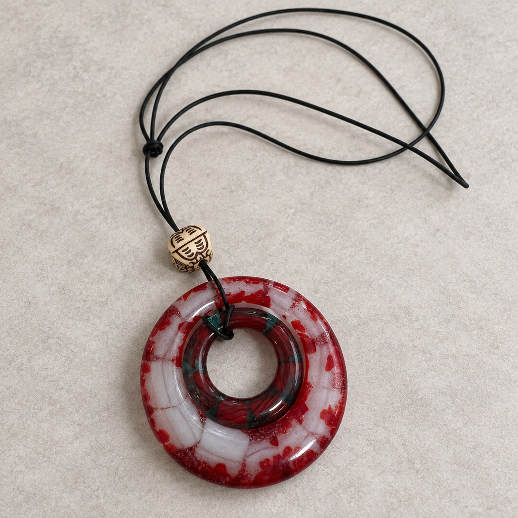 Red and white circular openwork glass pendant on a black cord