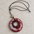 Red and white circular openwork glass pendant on a black cord