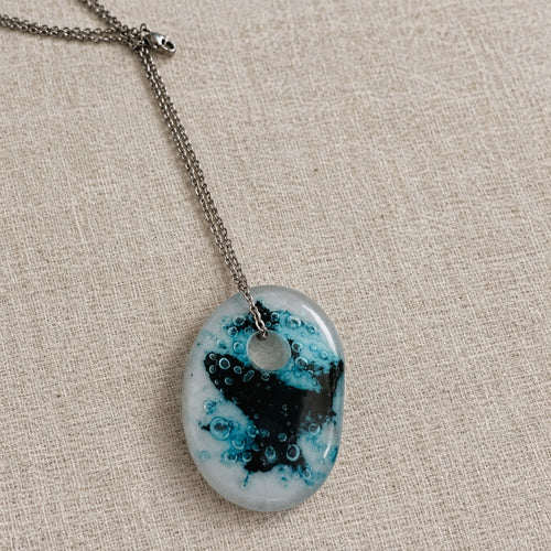 Pale oval glass pendant with blue and black patterned details on a chain