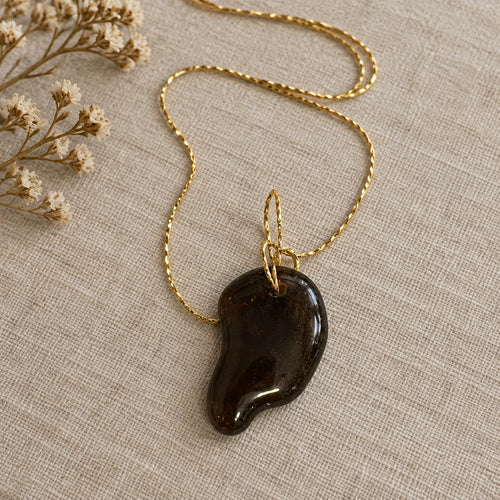 Dark curved glass pendant on a gold-colored chain