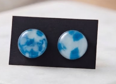 Pair of round blue and white glass stud earrings on a black display card