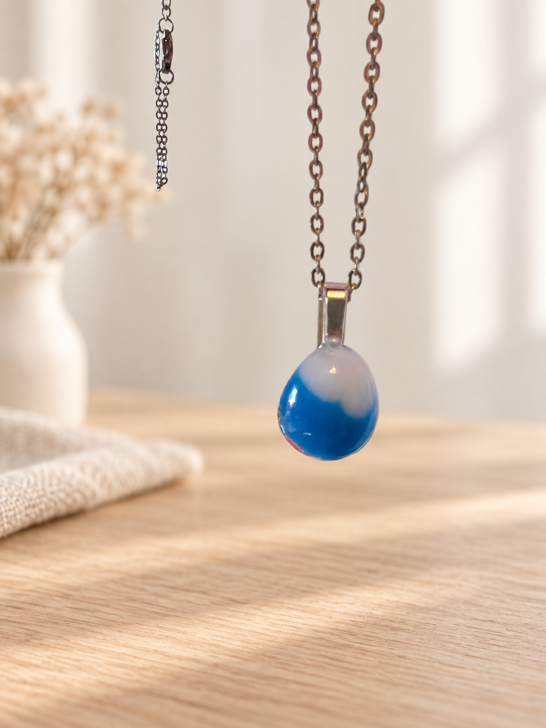 Blue and white glass teardrop pendant hanging from a chain