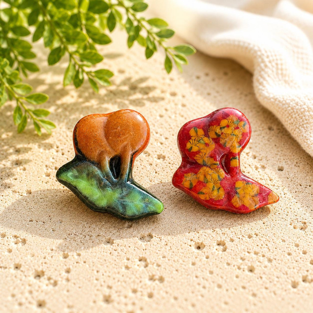 Two cat-shaped glass pieces, one orange and green and one red with multicolor details